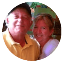 Two adults, a man in a yellow shirt and cap and a woman in a white top, smiling while posing together indoors.